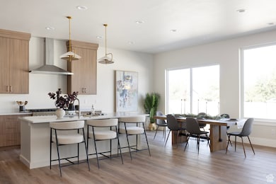 Kitchen with wall chimney exhaust hood, a kitchen bar, light stone countertops, light wood finished floors, and hanging light fixtures