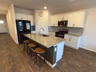 Kitchen featuring white cabinetry, decorative backsplash, appliances with stainless steel finishes, light stone countertops, and an island with sink