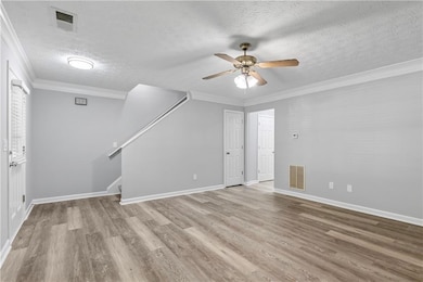 Unfurnished living room with a textured ceiling, ornamental molding, light wood-style floors, ceiling fan, and stairway