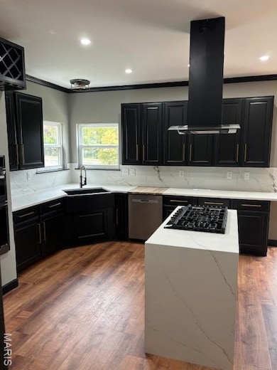 Kitchen featuring dark cabinetry, decorative backsplash, light stone countertops, dark wood-style flooring, and ornamental molding