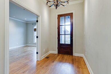 Foyer with custom light fixture and hardwood floors. Only two steps into the home and covered front porch.  View of front spare bedroom located off the foyer.  Crown molding and neutral colors throughout