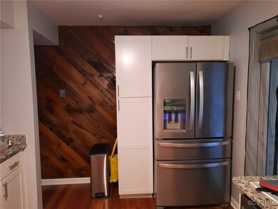 Kitchen with light stone counters, wood walls, stainless steel fridge with ice dispenser, and white cabinetry