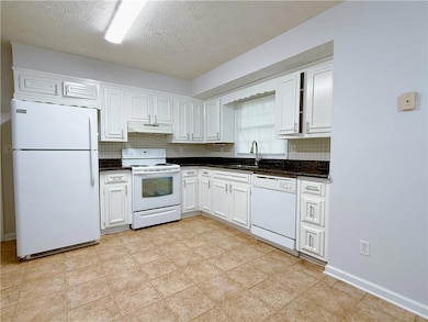 Kitchen featuring white appliances, under cabinet range hood, a sink, decorative backsplash, and white cabinets