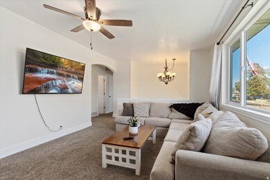 Carpeted living area featuring arched walkways, ceiling fan, and a chandelier