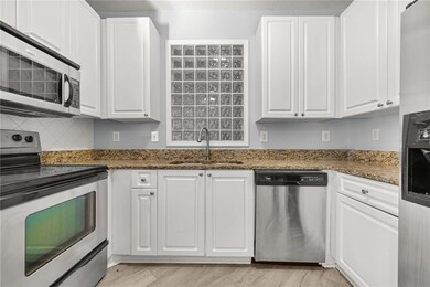 Kitchen with appliances with stainless steel finishes, dark stone countertops, white cabinets, light wood-style flooring, and backsplash
