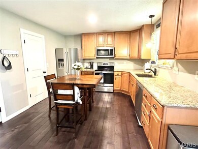 Kitchen with appliances with stainless steel finishes, dark wood-style flooring, light stone counters, and pendant lighting