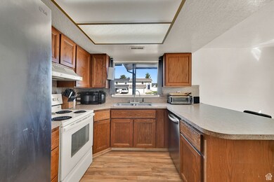 Kitchen featuring a peninsula, brown cabinetry, stainless steel appliances, and a textured ceiling