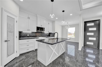 Kitchen featuring white cabinets, decorative backsplash, a kitchen island with sink, recessed lighting, and hanging light fixtures
