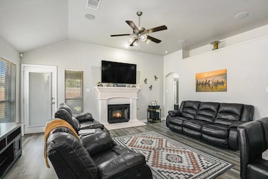 Living area featuring lofted ceiling, arched walkways, a warm lit fireplace, wood finished floors, and plenty of natural light