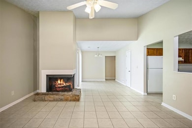 Unfurnished living room with a warm lit fireplace, a ceiling fan, light tile patterned flooring, and a high ceiling