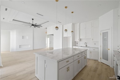Kitchen featuring backsplash, pendant lighting, white cabinets, a center island, and light wood-style flooring