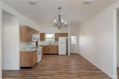 Kitchen with brown cabinetry, visible vents, white appliances, and a sink