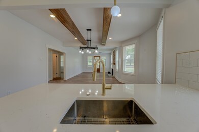 Kitchen view of a sink, beamed ceiling, decorative light fixtures, recessed lighting, and light stone countertops