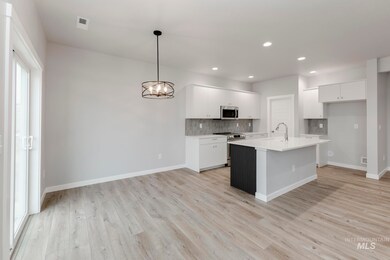 Kitchen featuring white cabinets, backsplash, appliances with stainless steel finishes, a chandelier, and a center island with sink