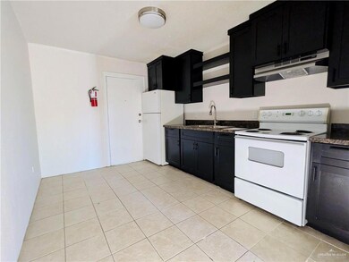 Kitchen with under cabinet range hood, white appliances, a sink, and dark cabinetry