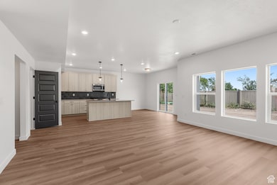 Kitchen with open floor plan, decorative backsplash, recessed lighting, an island with sink, and light wood-style floors