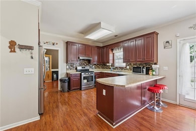Kitchen featuring appliances with stainless steel finishes, under cabinet range hood, a peninsula, backsplash, and crown molding
