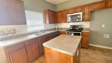 Kitchen featuring stainless steel appliances, a center island, decorative backsplash, a sink, and brown cabinetry