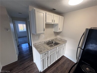 Kitchen featuring a baseboard heating unit, white cabinetry, sink, dark hardwood / wood-style flooring, and black refrigerator