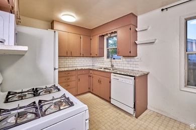 Kitchen with backsplash, white appliances, light floors, and light stone countertops