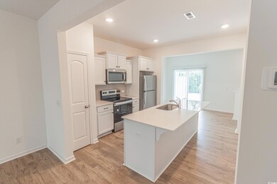 Kitchen featuring appliances with stainless steel finishes, a sink, a kitchen island with sink, white cabinetry, and light wood-type flooring