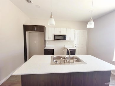 Kitchen with dark brown cabinets, stainless steel microwave, hanging light fixtures, and a kitchen island with sink