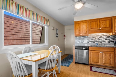 Kitchen featuring stainless steel dishwasher, a sink, light wood-style flooring, brown cabinets, and stone countertops