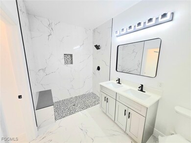 Bathroom featuring a marble finish shower, double vanity, and light marble finish floors