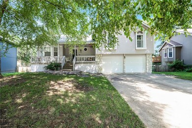 Tri-level home with covered porch, a garage, concrete driveway, stone siding, and a front lawn