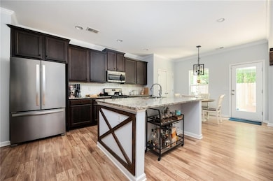 Kitchen with stainless steel appliances, decorative backsplash, ornamental molding, light stone countertops, and light wood-style floors