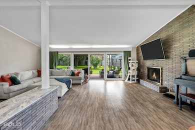 Living area with wood finished floors, vaulted ceiling, and a brick fireplace