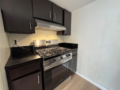 Kitchen featuring dark countertops, stainless steel range with gas stovetop, dark cabinetry, under cabinet range hood, and a textured ceiling