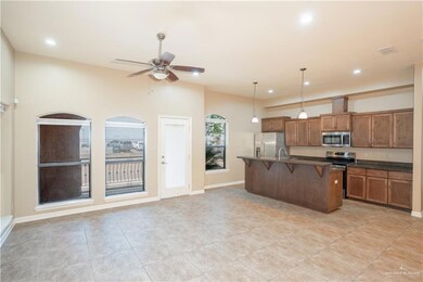 Kitchen with stainless steel appliances, brown cabinetry, a kitchen bar, a ceiling fan, and decorative light fixtures