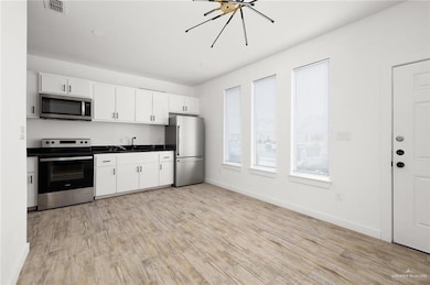 Kitchen featuring stainless steel appliances, light wood finished floors, dark countertops, and white cabinetry