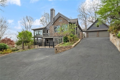 View of front facade featuring a gate, stone siding, a garage, asphalt driveway, and a chimney