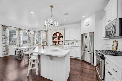 Kitchen featuring stainless steel appliances, white cabinets, a breakfast bar, a chandelier, and dark wood-type flooring