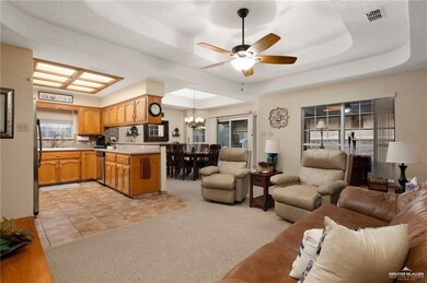 Living room with sink, light tile flooring, a raised ceiling, and ceiling fan with notable chandelier