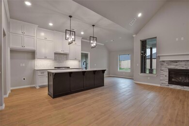 Kitchen featuring hanging light fixtures, light hardwood / wood-style floors, white cabinetry, and a stone fireplace