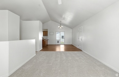 Unfurnished living room with light carpet, a chandelier, and lofted ceiling