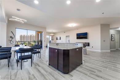 Kitchen featuring open floor plan, dark brown cabinets, light stone countertops, a center island, and recessed lighting