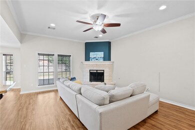 Living area featuring crown molding, light wood-type flooring, a stone fireplace, recessed lighting, and ceiling fan
