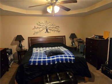 Bedroom with carpet floors, a raised ceiling, a textured ceiling, and a ceiling fan