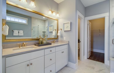 Bathroom featuring a shower stall, double vanity, marble look tiles, and a walk in closet