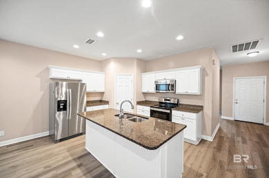 Kitchen with stainless steel appliances, light hardwood / wood-style floors, a center island with sink, sink, and white cabinets