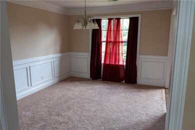 Carpeted spare room featuring a decorative wall, a chandelier, wainscoting, and crown molding