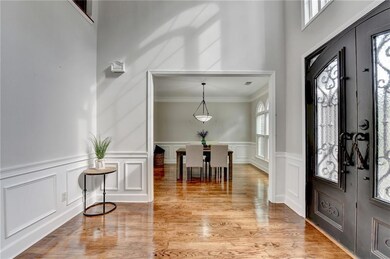 Entryway with a decorative wall, light wood finished floors, wainscoting, a towering ceiling, and crown molding