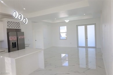 Kitchen with white cabinetry, stainless steel refrigerator with ice dispenser, light marble finish floors, a raised ceiling, and recessed lighting