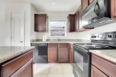 Kitchen with granite counters, black appliances, sink, and light tile floors