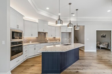 Kitchen featuring stainless steel appliances, a center island with sink, a tray ceiling, light wood-type flooring, and sink