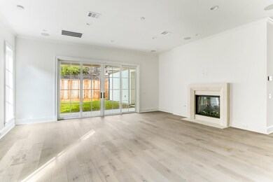 Stunning shot of the family room boasts elegance with the custom cast stone mantel for the gas-log fireplace and lovely white oak hardwoods. Notice the beautiful sliding doors that overlook the side garden as well as provide ample natural light throughout.